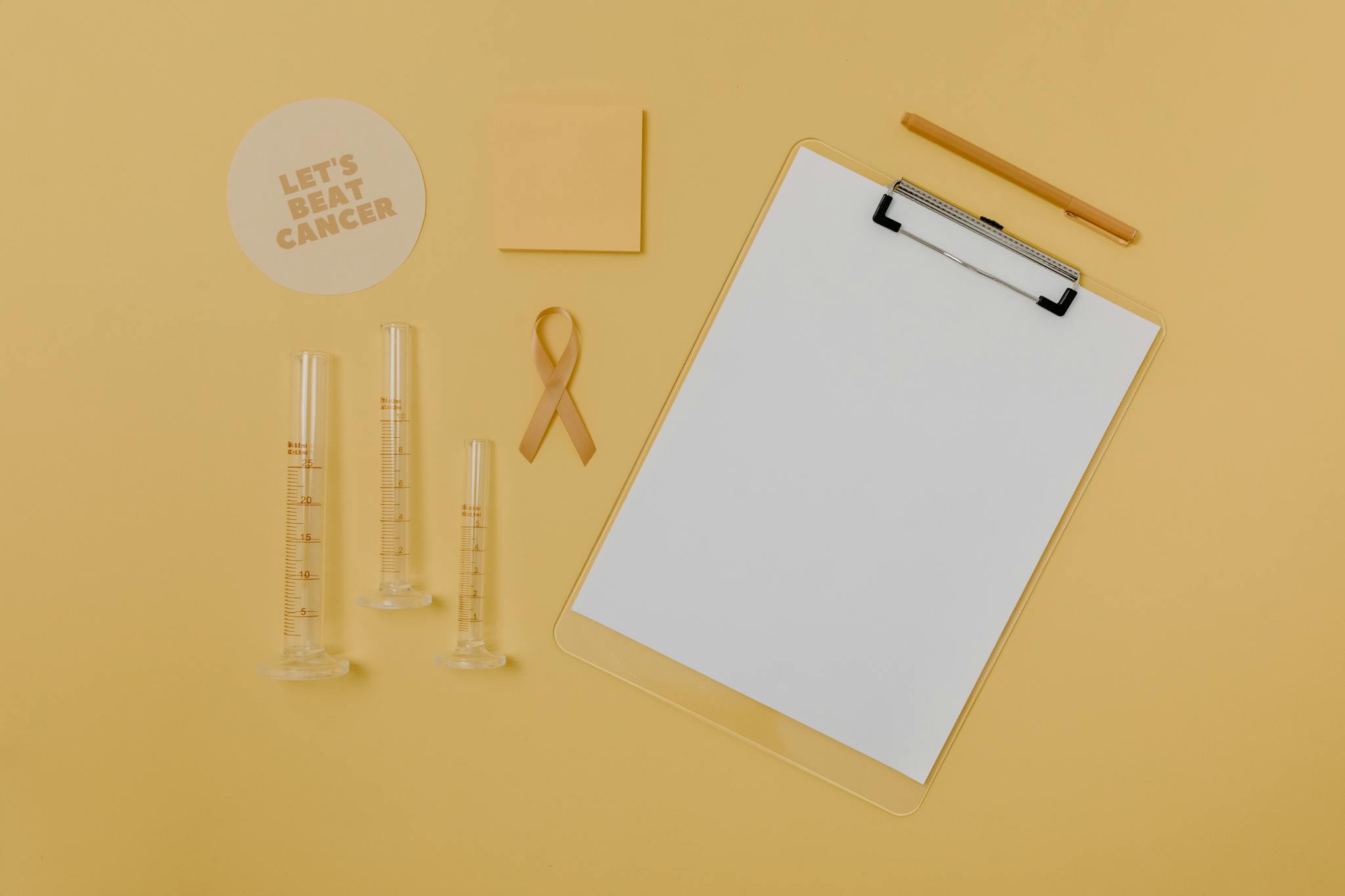 Flat lay of medical tools and cancer awareness ribbon on yellow background.